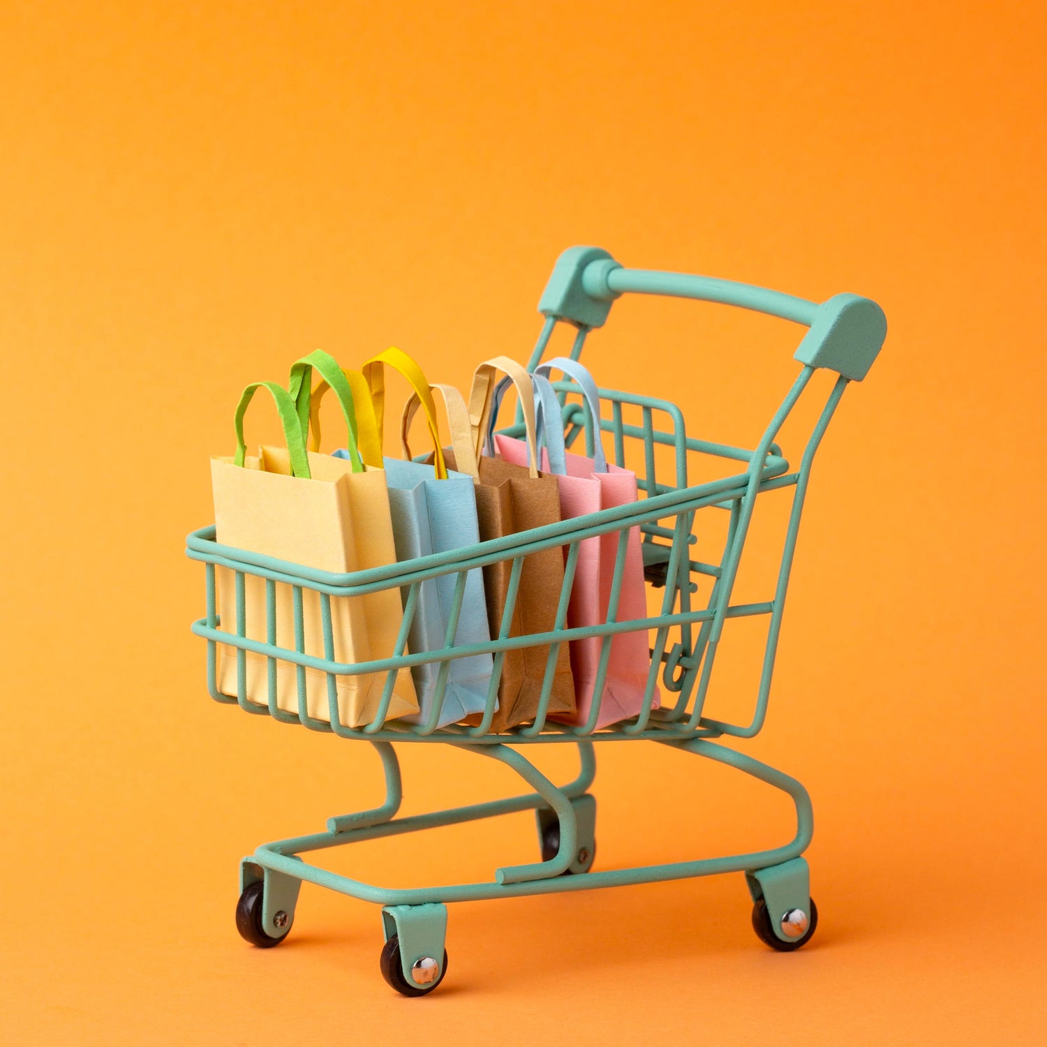 Small shopping cart filled with colorful paper bags on an orange background