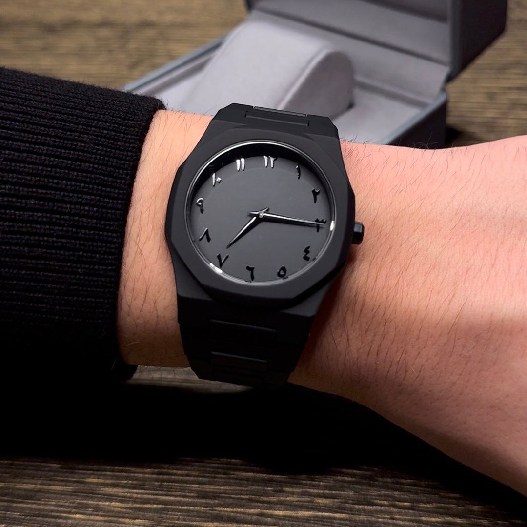 Black wristwatch on a person's wrist with a wooden surface in the background